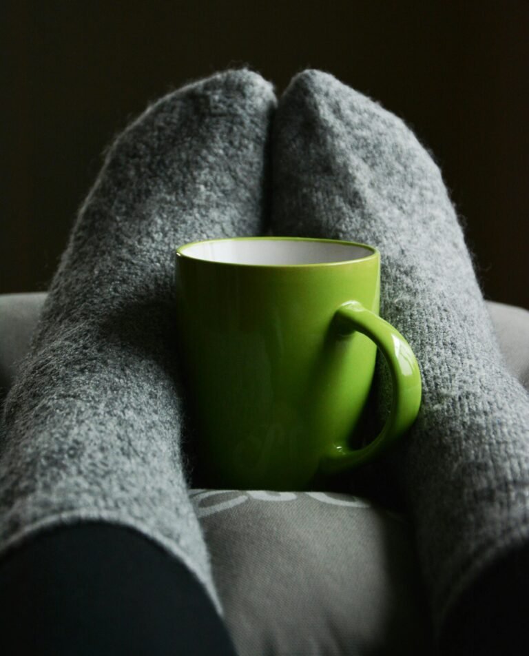 Warm and cozy indoor scene with a green mug between gray wool socks, perfect for relaxation.